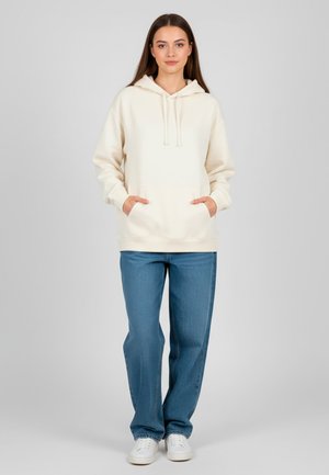 Crème hoodie met een kangoeroezak, trekkoordcapuchon en ribgebreide manchetten, gecombineerd met losse blauwe denim jeans en witte sneakers.