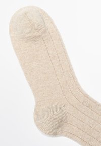 Beige gestrickte Socke mit einer gerippten Struktur, die subtile Streifen und eine abgerundete Zehe aufweist. Weiches Aussehen mit einem gemütlichen, warmen Eindruck.