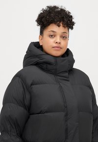 Black puffer jacket with a high collar and quilted design. Made from glossy, padded material, featuring a front zipper and subtle branding.