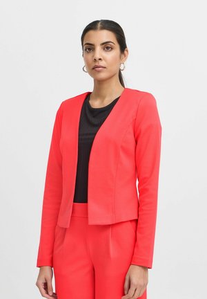 Roter Blazer mit einem glatten, taillierten Design, das einen runden Ausschnitt und eine offene Front aufweist. Getragen über einem schwarzen, gerippten Oberteil, ergänzt durch eine Hose.