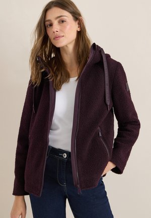Burgunderfarbener Fleece-Jacke mit Reißverschluss, zwei seitlichen Taschen und Kapuze. Mit glattem Innenfutter und Kordelzug-Detail, getragen über einem weißen Hemd.