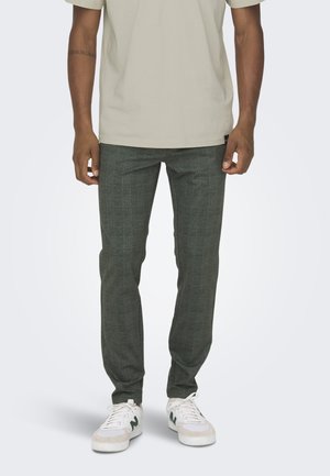 Pantalones de cuadros verde oscuro hechos de tela ligera, con un corte ajustado, combinados con zapatillas blancas y una camiseta beige.