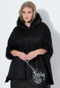 Abrigo negro con capucha de piel, mangas de murciélago y cintura ceñida con cinturón. Acompañado de un bolso redondo brillante con lentejuelas.