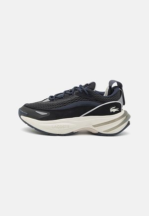 Zapatillas para hombre de Lacoste con parte superior de malla negra y azul marino, acentos grises, suela intermedia blanca y gruesa, y un tirador trasero para facilitar su uso.