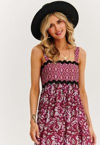 Sukienka w kwiatowy wzór w kolorach fioletowym i białym, z dopasowanym gorsetem wykończonym czarną falbanką oraz cienkimi ramiączkami, przechodzącą w luźną spódnicę.