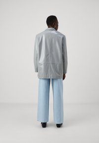 Palton oversized gri, lucios, cu mâneci lungi și croi drept, asortat cu blugi largi de culoare bleu deschis. Textură netedă, design minimal.