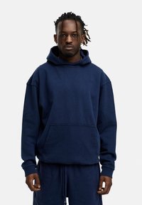 Dunkelblaues Baumwoll-Hoodie mit einer Fronttasche, Kapuze mit Kordelzug und gerippten Bündchen, kombiniert mit passenden dunkelblauen Hosen.