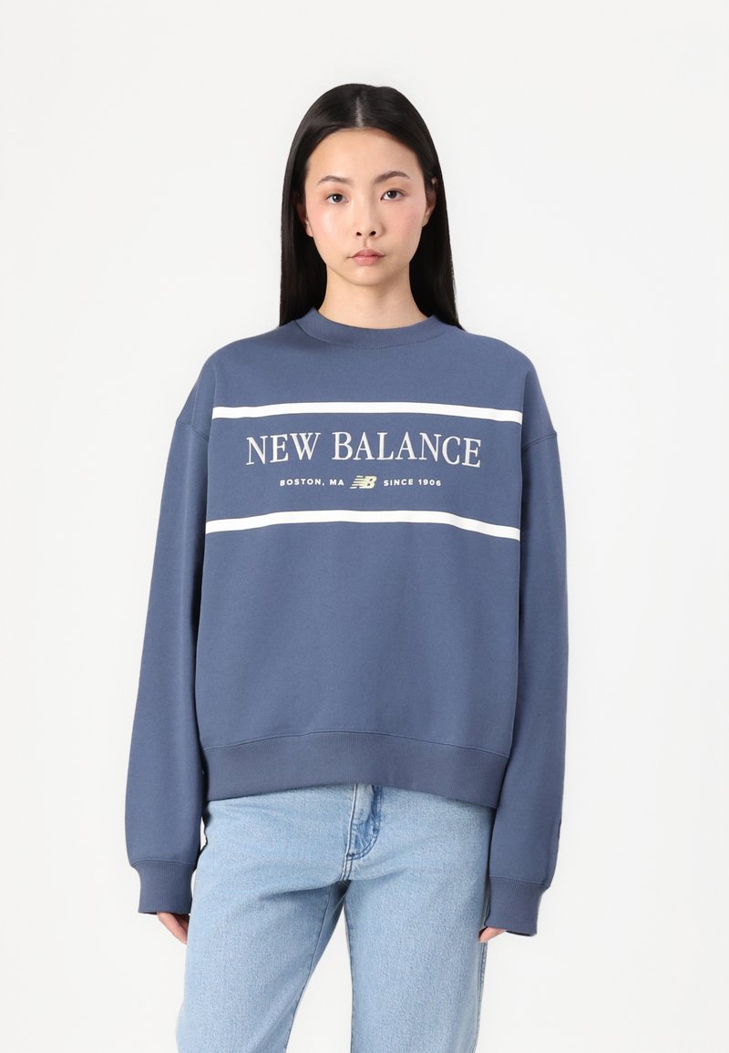 Blue sweatshirt with white horizontal stripes, "NEW BALANCE" logo and text on the front. Loose fit with ribbed cuffs and hem.