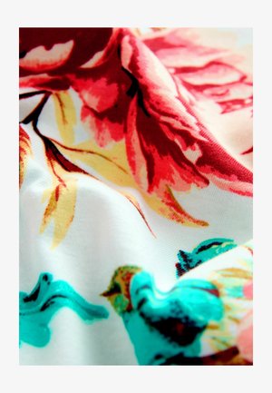 Tissu fleuri avec de grandes fleurs roses et rouges aux accents jaunes, sur un fond blanc. Texture lisse avec des couleurs et des motifs vibrants.