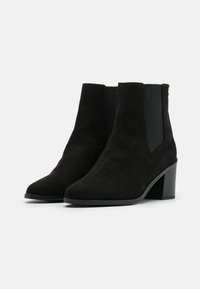 Stivaletti alla caviglia in suede nero con punta appuntita, pannelli laterali elastici e tacco impilato. Texture liscia e design minimalista.