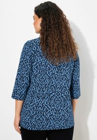 Modrý vzorovaný top s tmavým pozadím a světlými modrými vzory, tříčtvrteční rukávy a zaoblený lem. Texturovaná tkanina.