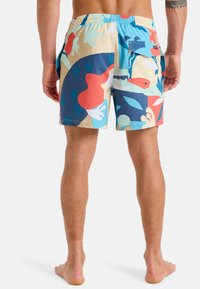 Bunt gemusterte Badekürze mit einer Mischung aus abstrakten Formen in Blau, Rot und verschiedenen Pastelltönen. Elastischer Bund mit Taschen.