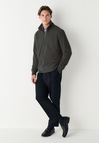 Tumši pelēks rāvējslēdzēja džemperis, melnas brīva piegriezuma bikses un melni loafers ar zelta akcentiem. Gluda tekstūra, ikdienišķs dizains.