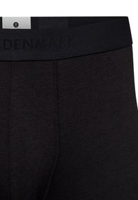 Musta alusvaate, jossa on pehmeä vyötärö, johon on kohokuvioitu "DENMARK". Kangas näyttää sileältä, tiukalta ja siinä on minimaalinen ommeltyyli.