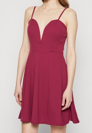 Vestido burdeos con un escote en V profundo, tirantes finos y falda acampanada. Hecho de un tejido elástico, presenta una superficie lisa y sin textura.