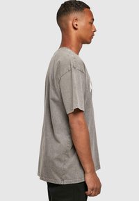 Grijze t-shirt met korte mouwen en een relaxte pasvorm, voorzien van een vervaagde textuur en zichtbare stikdetails, gedragen met zwarte broek.