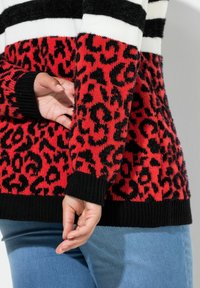 Roter und schwarzer Leopardenmuster-Strickpullover mit weißen und schwarzen gestreiften Akzenten; mit gerippten Bündchen und Saum ausgestattet; weicher Stoff.