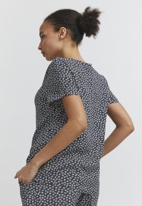 Haut à imprimé floral noir et blanc, manches courtes, col rond, tissu léger, coupe décontractée, détail de pli au dos, texture lisse.
