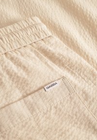 Beežikas tekstureeritud kangas pehme, elastse vöökohaga ja tagataskuga, millel on väike „GABBA“ silt.