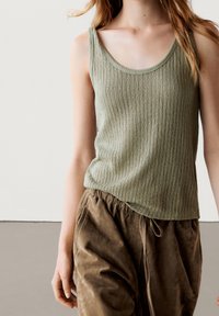 Olivgrön ribbad tanktop med rundad halsringning, kombinerad med lösa bruna byxor med elastisk midja och dragsko.