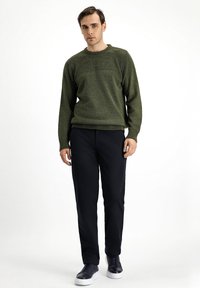 Suéter verde de punto con textura acanalada en el cuello, combinado con pantalones negros y zapatillas azul marino. Ajuste simple y casual.
