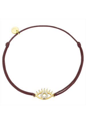 Goldener, augenförmiger Anhänger mit einem klaren Stein in der Mitte, montiert an einem geflochtenen bordeauxfarbenen Band mit einem Knoten und einem runden goldenen Etikett.