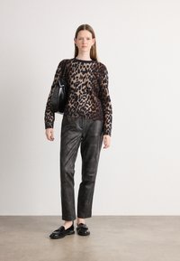 Pull en imprimé léopard beige, marron et noir ; pantalon en cuir noir ; mocassins noirs ; sac noir uni avec une petite étiquette.