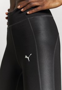 Czarne legginsy sportowe o gładkiej, błyszczącej strukturze. Posiadają kontrastowe przeszycia oraz białe logo Pumy na lewej udzie.