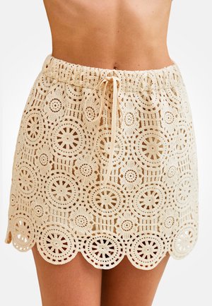 Mini gonna beige all'uncinetto con motivi floreali circolari e orlo smerlato, dotata di una cintura elastica con coulisse annodata.