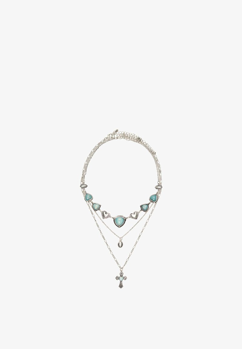 Ezüst többrétegű nyaklánc türkiz szív alakú kövekkel, egy kis ovális medállal és egy részletes kereszt medállal fehér háttéren.