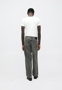 Παντελόνι τζιν γκρί, φαρδ�ύ με ψηλή μέση και πέντε τσέπες, σε συνδυασμό με ένα απλό λευκό κοντομάνικο μπλουζάκι, σε προβολή από πίσω.