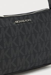 Black handbag featuring a textured exterior with a repeating logo pattern, silver hardware, and a zip closure.