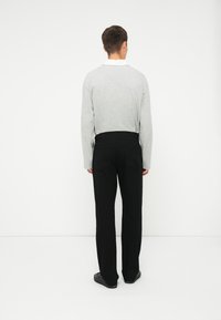 Grijze langemouwenshirt met een witte kraag, gecombineerd met zwarte recht-toe-rechtdoor-pants. De stof lijkt zacht; de outfit heeft een eenvoudig, strak ontwerp.