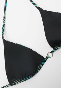Top de bikini negro con tirantes ajustables que presenta acentos de patrones en turquesa y negro; incluye un detalle de anillo de metal dorado en el centro.
