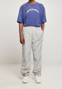 Lilla oversize t-shirt med udskæringer og "URBAN CLASSIC" trykt i hvid. Lysegrå joggers med elastik i taljen, hvide sneakers.