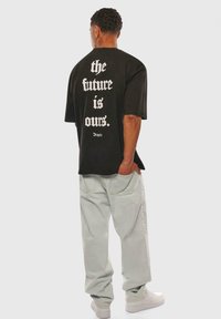 Black oversized t-shirt with large white printed text on the back. Paired with light-colored baggy pants and white sneakers.