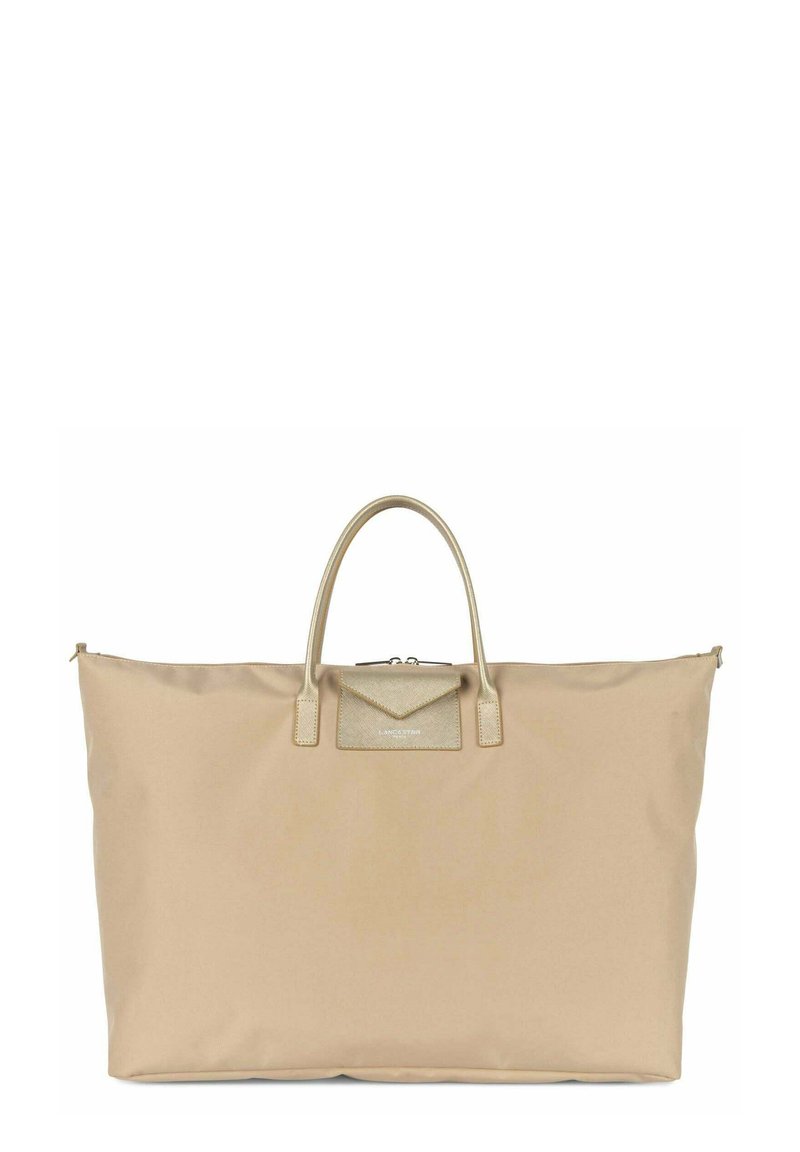 Sac fourre-tout en tissu doux beige avec deux poignées, une fermeture zippée et une poche accentuée en or texturé sur le devant. Design durable et spacieux.