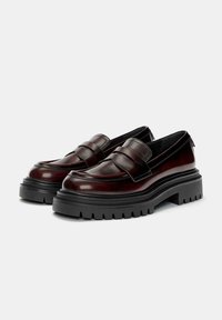 Pair of polished dark brown leather loafers with chunky black lug soles, rounded toes, and strap detailing across the top.