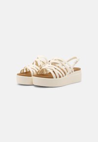 Bílé platformové sandály s propletenými pásky. Materiál se zdá být flexibilní s hladkým povrchem. Světle hnědá stélka kontrastuje s podešví.