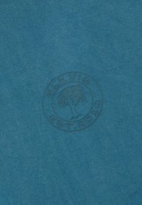 Niebieska tkanina z subtelny okrągłym logo "BLKVIG COTTON" z drzewem w centrum.