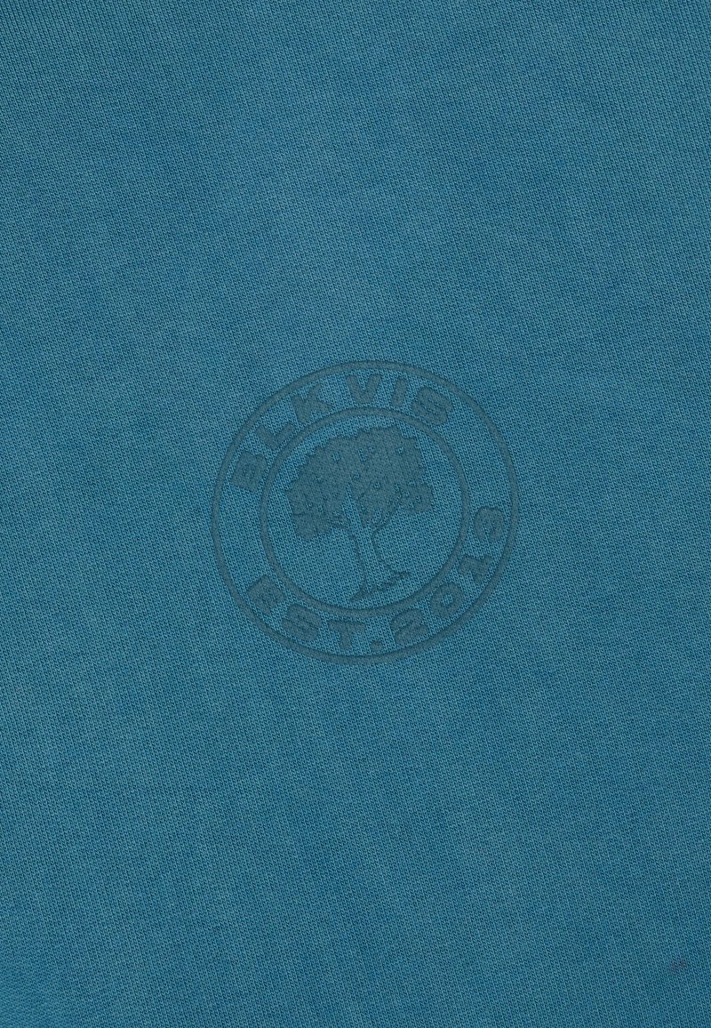 Niebieska tkanina z subtelny okrągłym logo "BLKVIG COTTON" z drzewem w centrum.