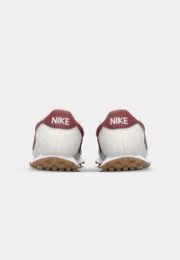 Červené a sivé športové tenisky Nike s textúrovanou semišovou pätou a gumovou podrážkou. Obsahujú výrazné logo na patách.