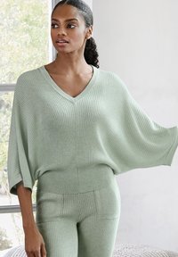 Mintgroen gebreid top met V-hals en brede mouwen, gecombineerd met bijpassende geribde broeken met zijzakken en textuurdetails.