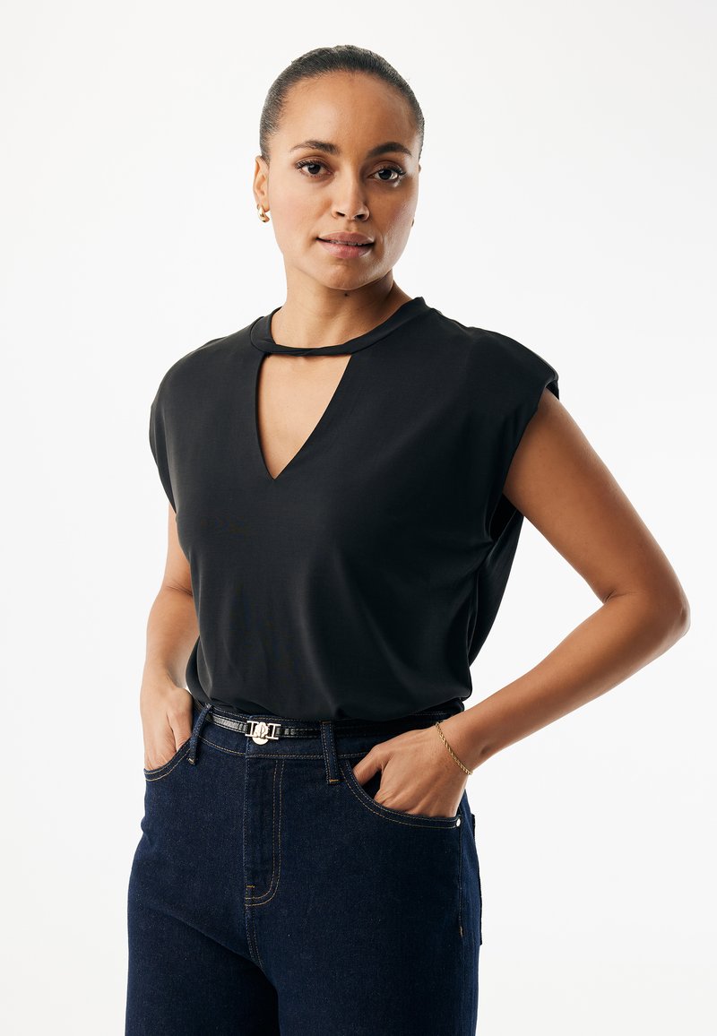 Schwarzes Kurzarmoberteil mit V-Ausschnitt und schmalem Ausschnitt, kombiniert mit dunkler Denim-Jeans und einem schwarzen Gürtel mit silberner Schnalle.