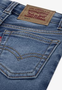 Világoskék farmernadrág bőr címkével, rajta a "LEVI STRAUSS & CO." felirat, valamint varrásdíszekkel. Klasszikus hátsó zsebminta jellemzi.