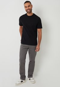 Schwarzes T-Shirt mit Rundhalsausschnitt und kurzen Ärmeln, kombiniert mit hellgrauen Hosen und weißen Sneakern mit schwarzen Akzenten. Glatte Stofftextur.