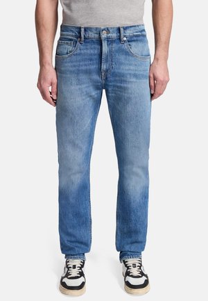 Lichtblauwe spijkerbroek met een recht model, vijf zakken, zichtbare stiksels en een versleten effect, gecombineerd met zwart-witte sneakers.