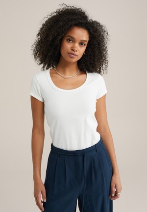 Weißes T-Shirt mit kurzen Ärmeln und weitem Ausschnitt, getragen mit dunkelblauen, hoch taillierten Hosen. Glatte Textur und taillierte Passform.