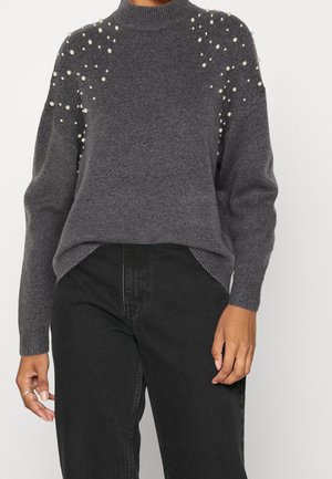 Grafitowoszary sweter z wysokim kołnierzem, ozdobiony rozproszonymi białymi perłami na ramionach, w połączeniu z czarnymi spodniami z wysokim stanem.