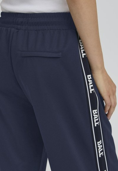 Pantalons de jogging navy avec une taille élastique, des bandes logo sur les côtés et une poche arrière. Fabriqués en tissu lisse, avec des accents blancs.